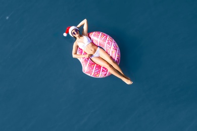 Young woman wearing Santa hat and bikini with inflatable ring in sea, top view. Christmas vacation