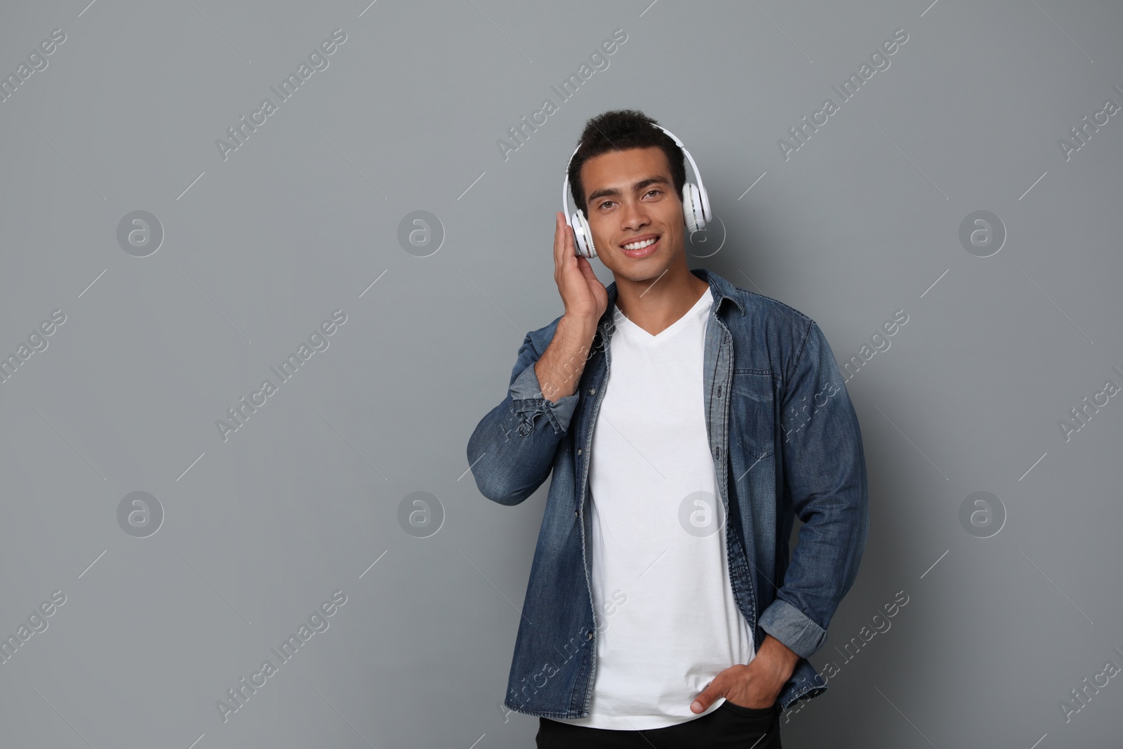 Photo of Handsome young African-American man with headphones listening to music against grey background. Space for text