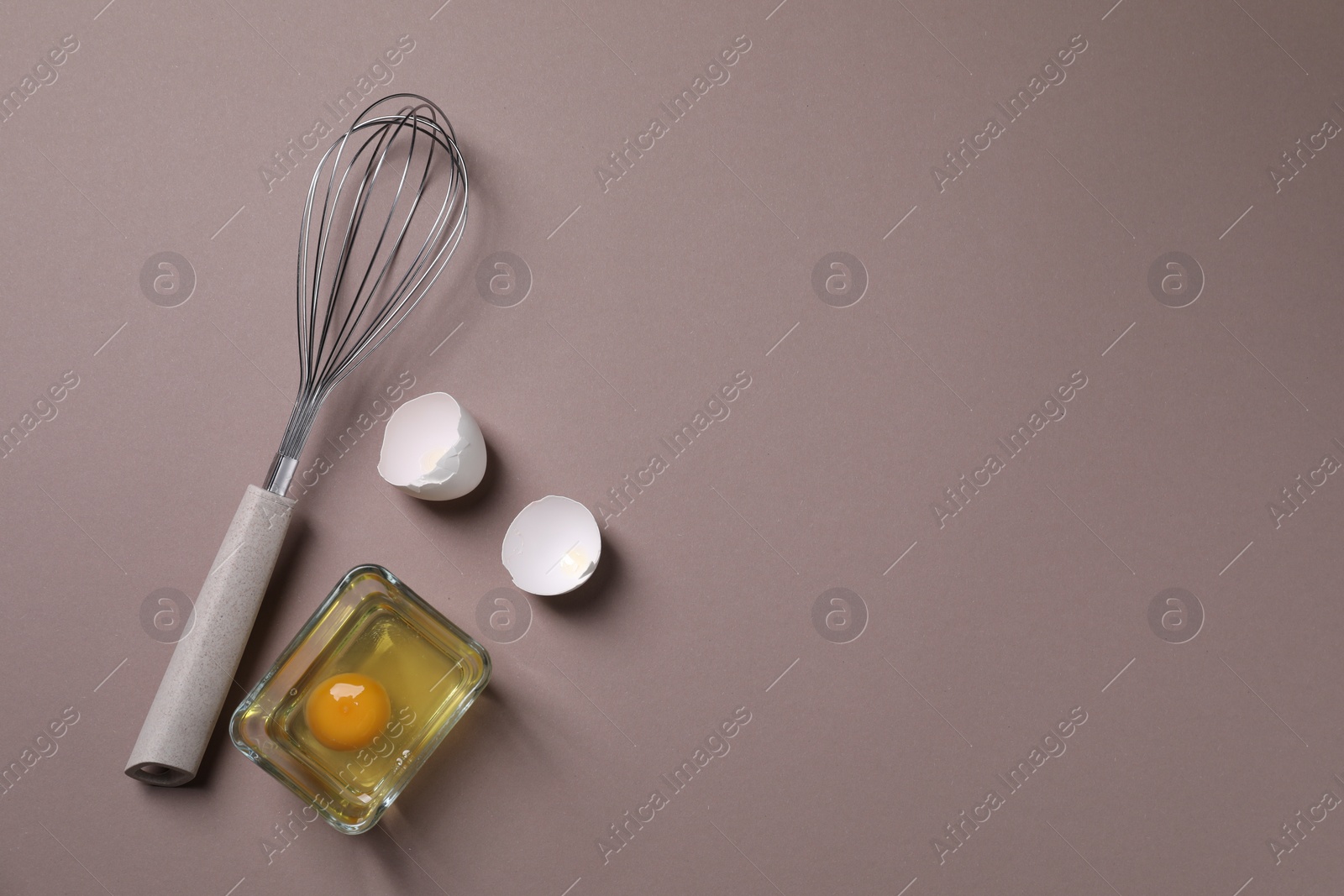 Photo of Metal whisk, raw egg in bowl and shells on grey background, flat lay. Space for text