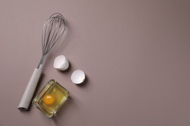 Photo of Metal whisk, raw egg in bowl and shells on grey background, flat lay. Space for text