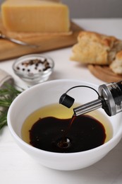 Photo of Pouring balsamic vinegar into bowl with oil on white table, closeup