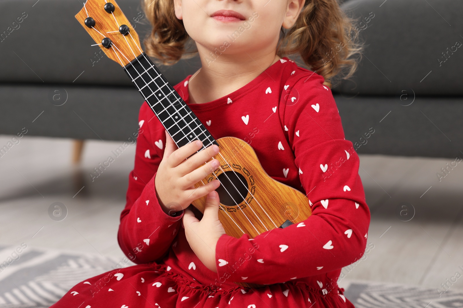 Photo of Little girl playing toy guitar at home, closeup