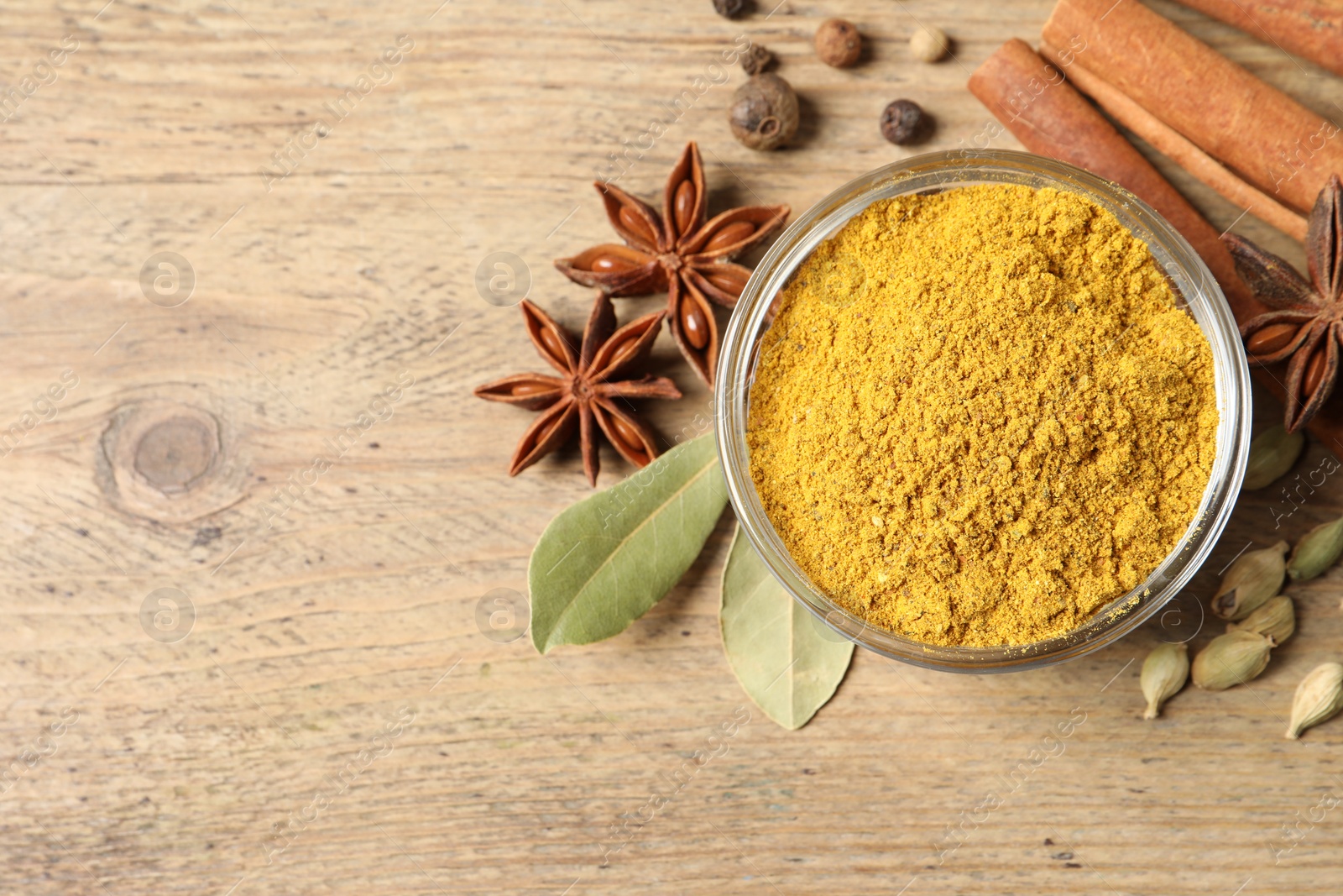 Photo of Curry powder in bowl and other spices on wooden table, flat lay. Space for text