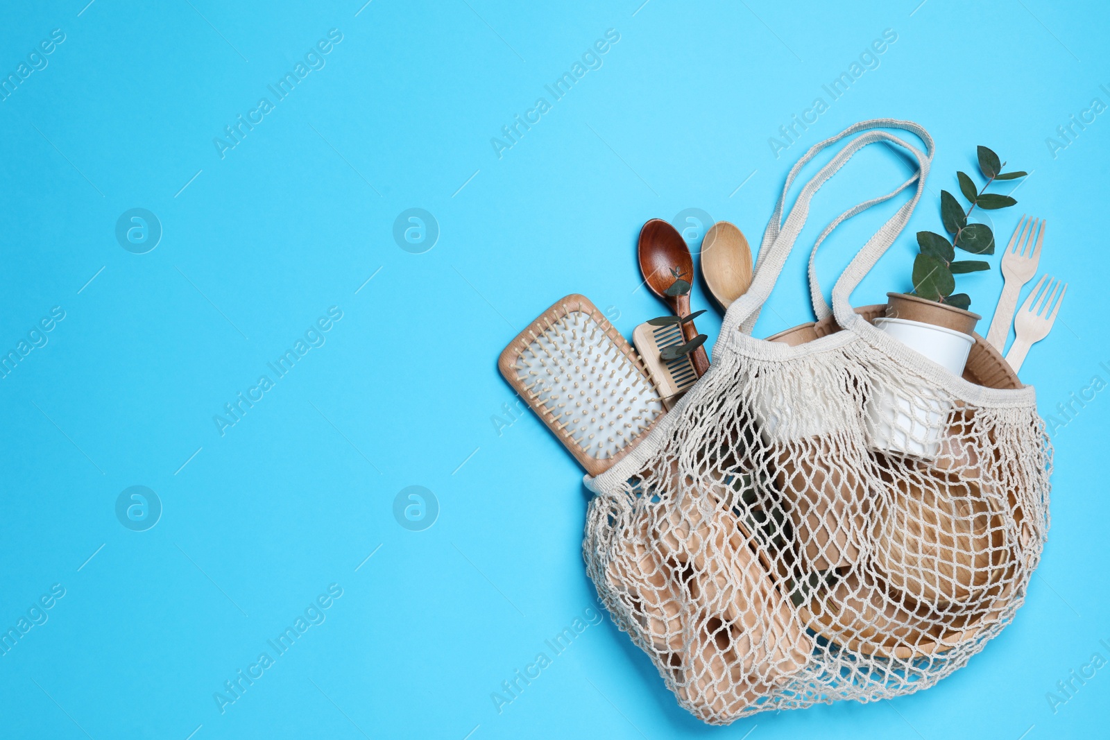 Photo of Net bag with different eco items on light blue background, top view and space for text. Recycling concept