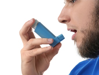 Young man using asthma inhaler on white background, closeup