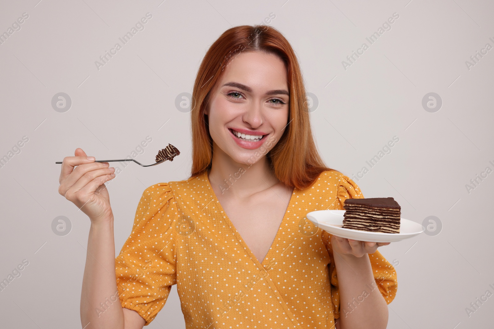 Photo of Young woman eating piece of tasty cake on light grey background