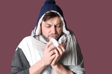 Man in warm clothes suffering from cold on color background