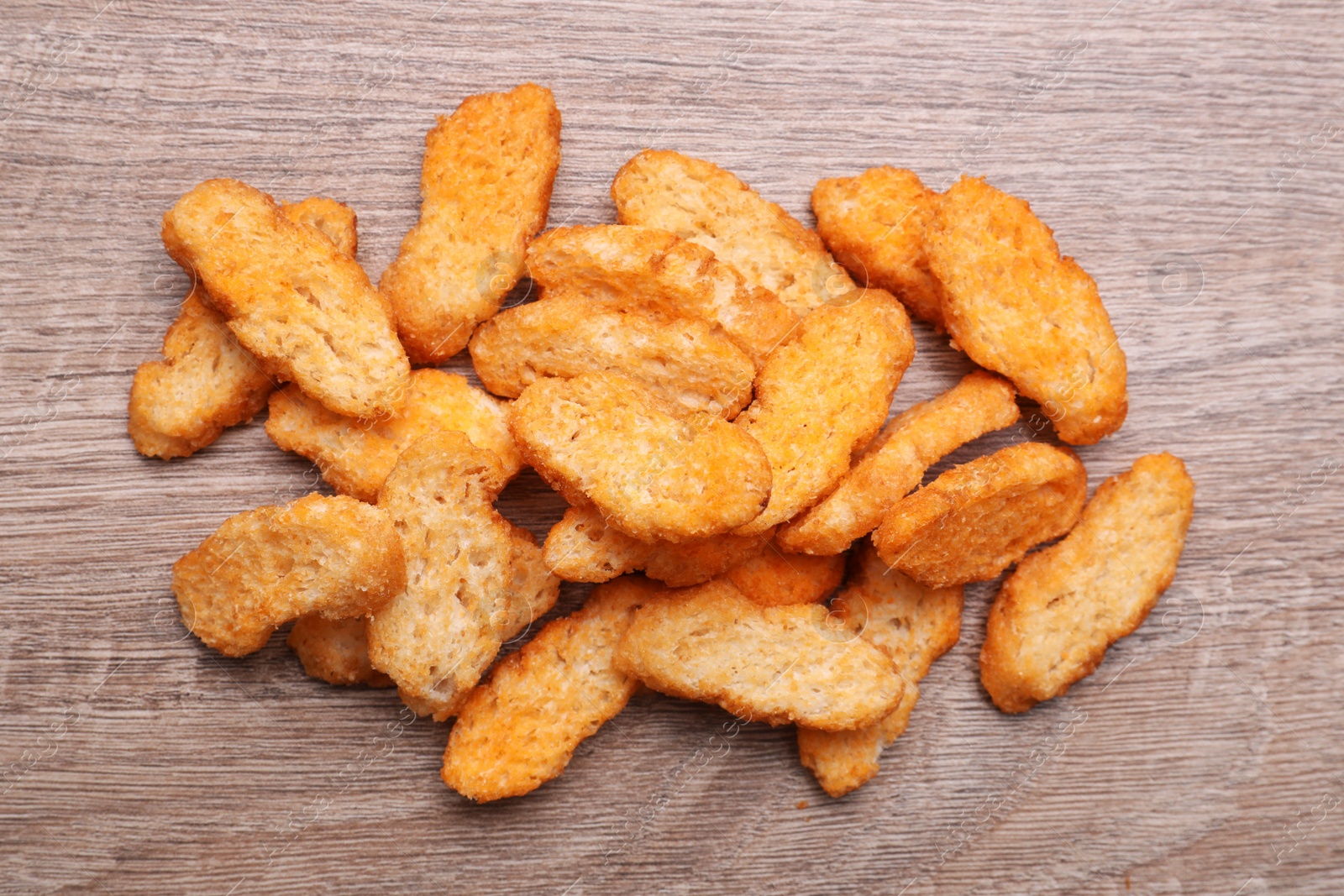 Photo of Heap of crispy rusks on wooden table, flat lay