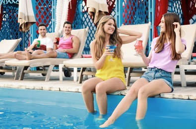 Happy young friends with fresh summer cocktails relaxing near swimming pool