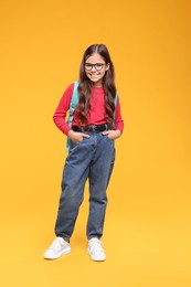 Photo of Cute schoolgirl in glasses on orange background