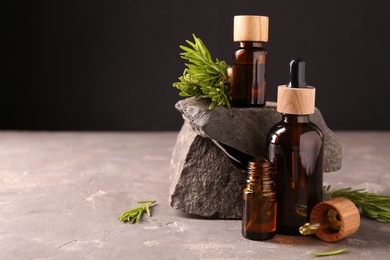 Photo of Essential oil in bottles, dropper and rosemary on grey table, space for text