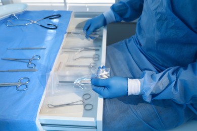 Photo of Doctor putting medical forceps into drawer indoors, closeup. Table with different surgical instruments