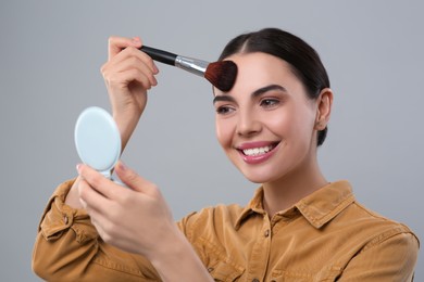 Photo of Happy woman with cosmetic pocket mirror applying makeup on light grey background