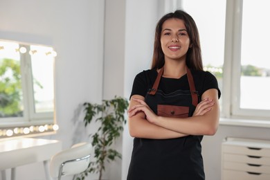 Photo of Portrait of happy hairdresser with professional apron in beauty salon. Space for text