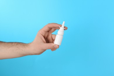 Photo of Man holding nasal spray on light blue background, closeup. Space for text