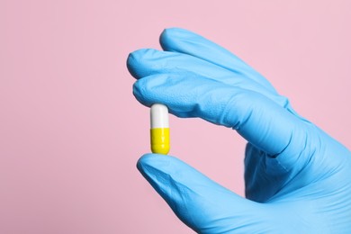 Photo of Doctor holding pill on pink background, closeup. Space for text