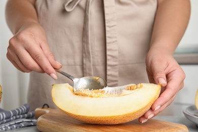 Young woman removing seeds from ripe melon with spoon at table, closeup