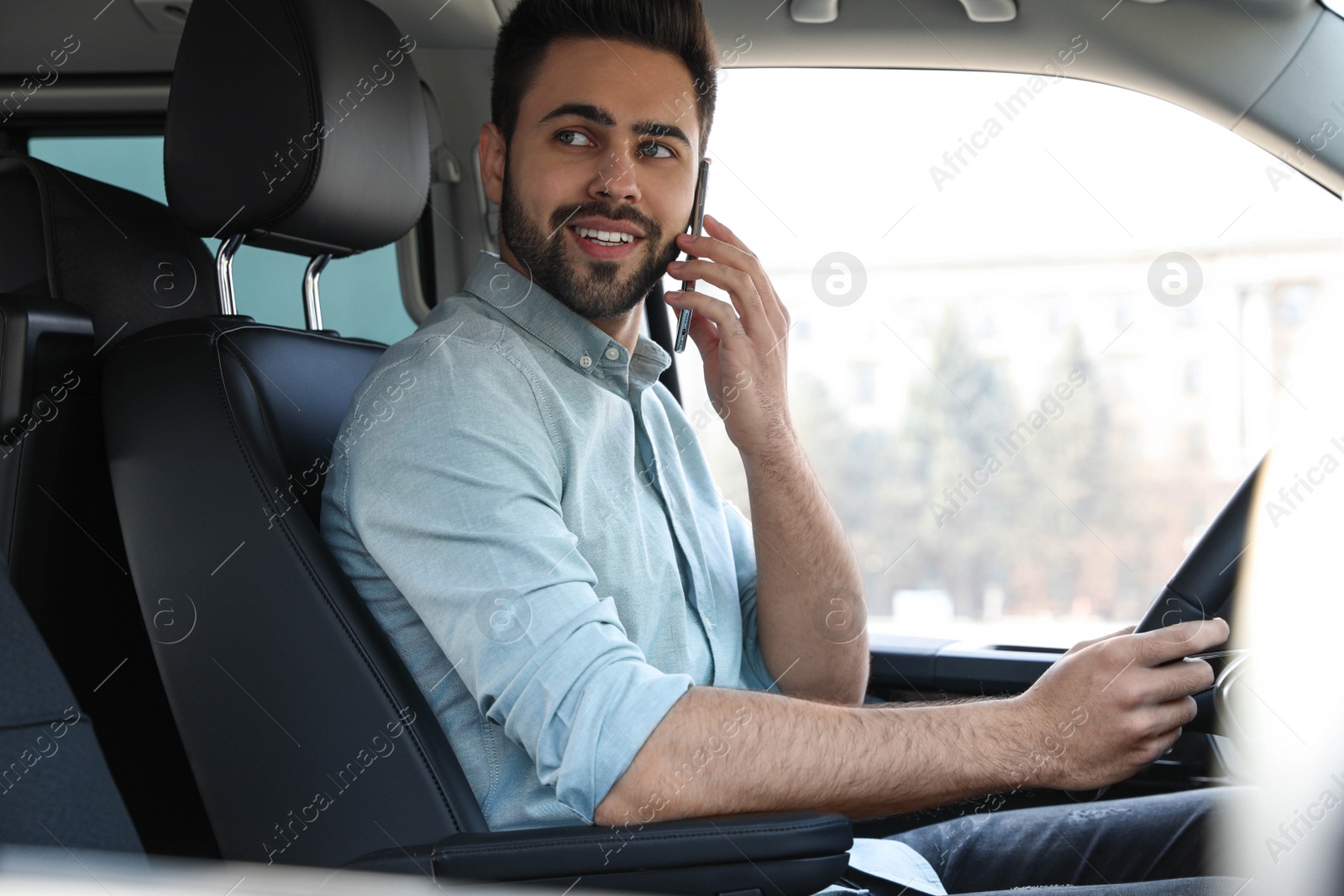 Photo of Handsome young man talking on smartphone while driving his car