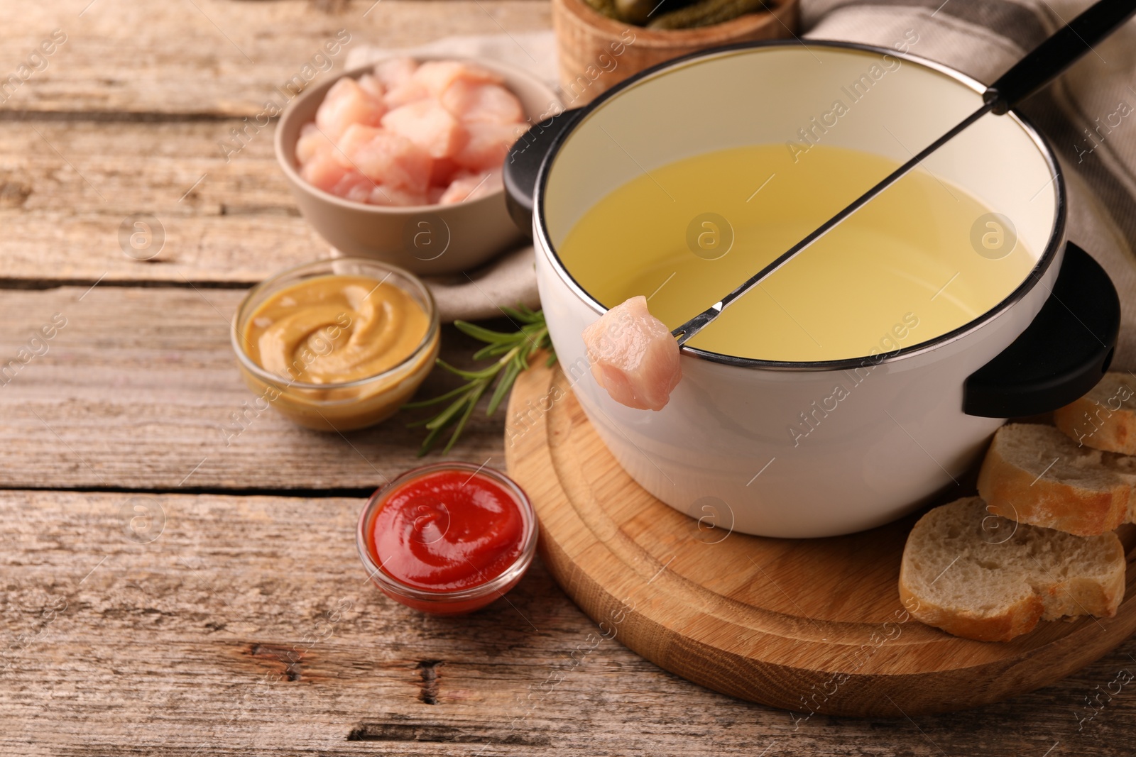 Photo of Fondue pot with oil, fork, raw meat pieces and other products on wooden table. Space for text