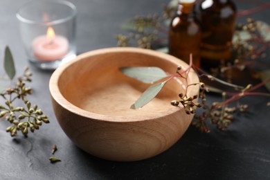 Photo of Wooden bowl, essential oil, eucalyptus branches and burning candle on grey table, closeup