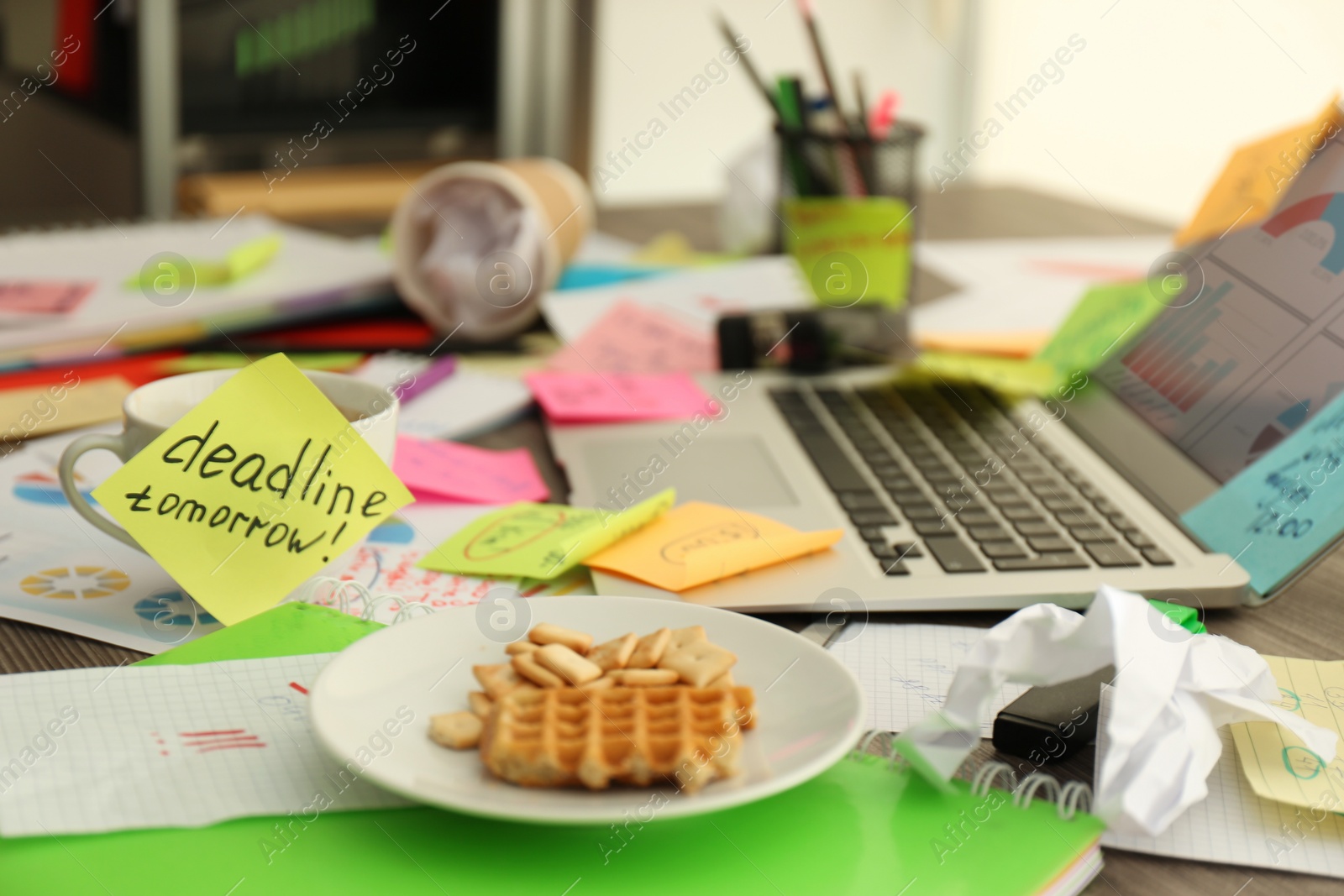 Photo of Laptop, notes and office stationery in mess on desk. Overwhelmed with work