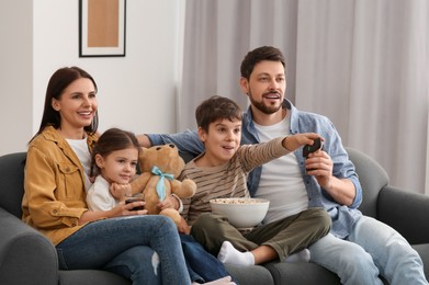 Photo of Happy family watching TV at home. Son changing channels with remote control