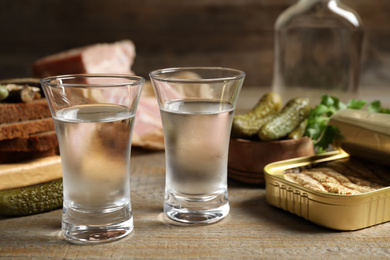 Photo of Cold Russian vodka with snacks on wooden table, closeup