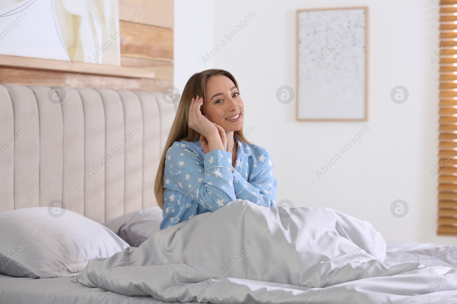Photo of Young woman sitting on comfortable bed with silky linens