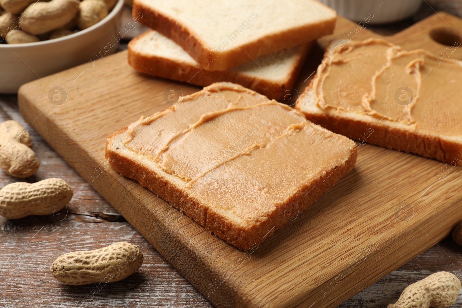 Photo of Tasty peanut butter sandwiches and peanuts on wooden table, closeup