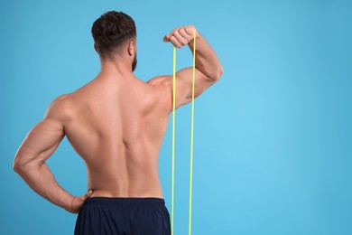 Photo of Young man exercising with elastic resistance band on light blue background, back view. Space for text