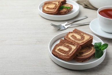 Photo of Tasty chocolate cake roll with cream and mint on light wooden table, space for text