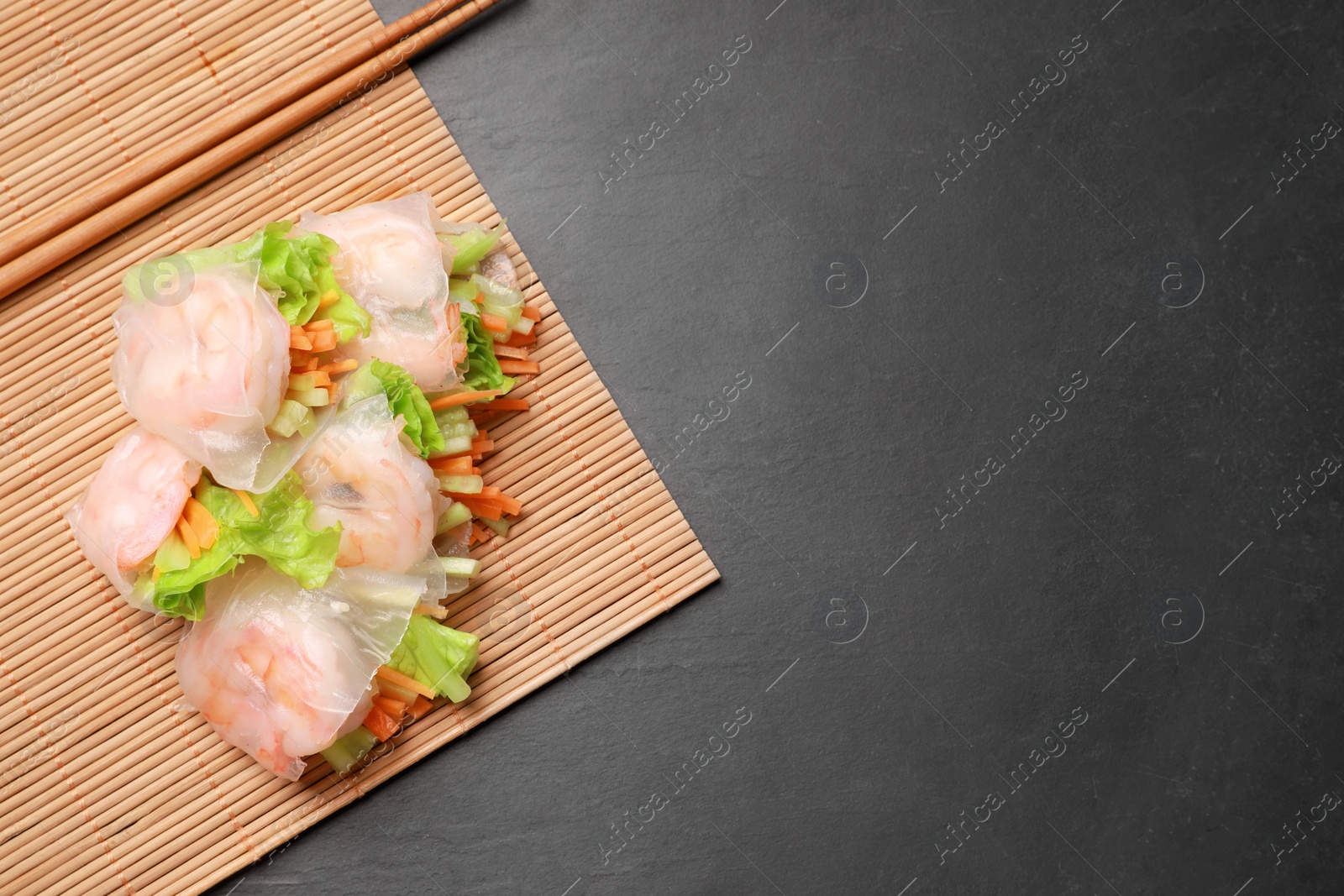 Photo of Tasty spring rolls, chopsticks and bamboo mat on grey textured table, top view. Space for text