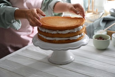 Photo of Woman stacking homemade sponge cakes at white wooden table, closeup