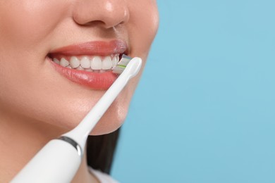 Photo of Woman brushing her teeth with electric toothbrush on light blue background, closeup. Space for text