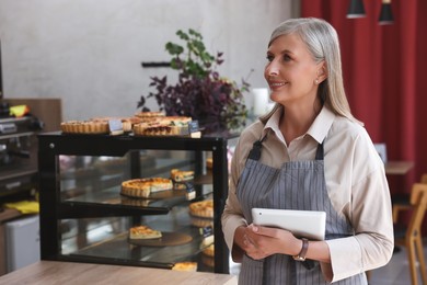 Happy business owner with tablet in her cafe, space for text