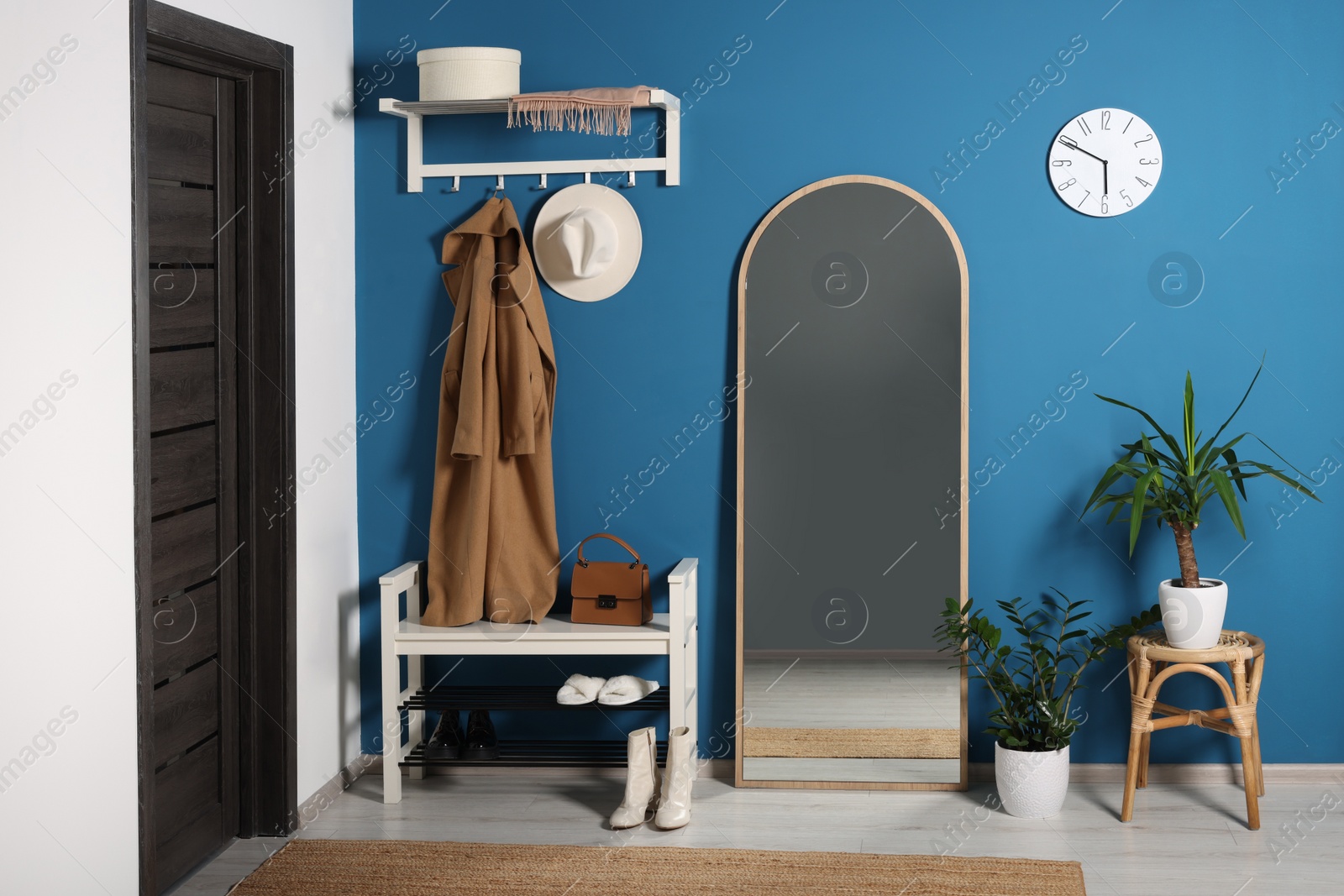 Photo of Stylish hallway with shoe storage bench and mirror near blue wall. Interior design