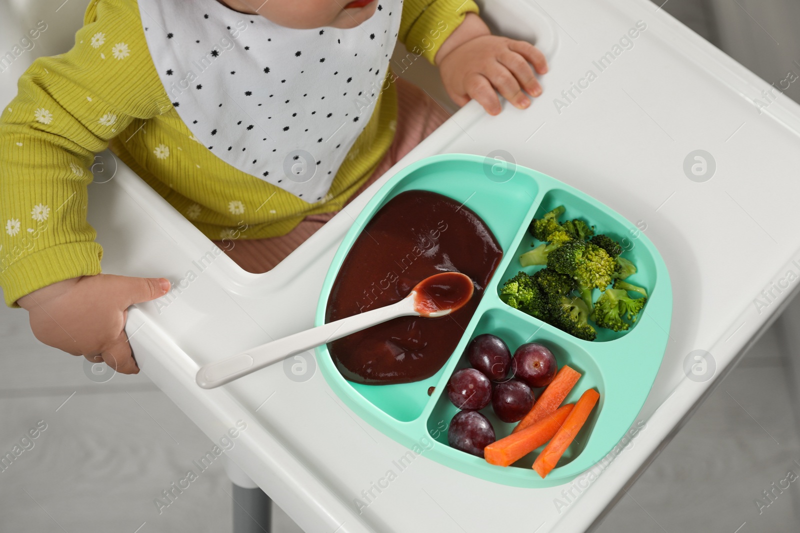 Photo of Cute little baby wearing bib while eating indoors, above view