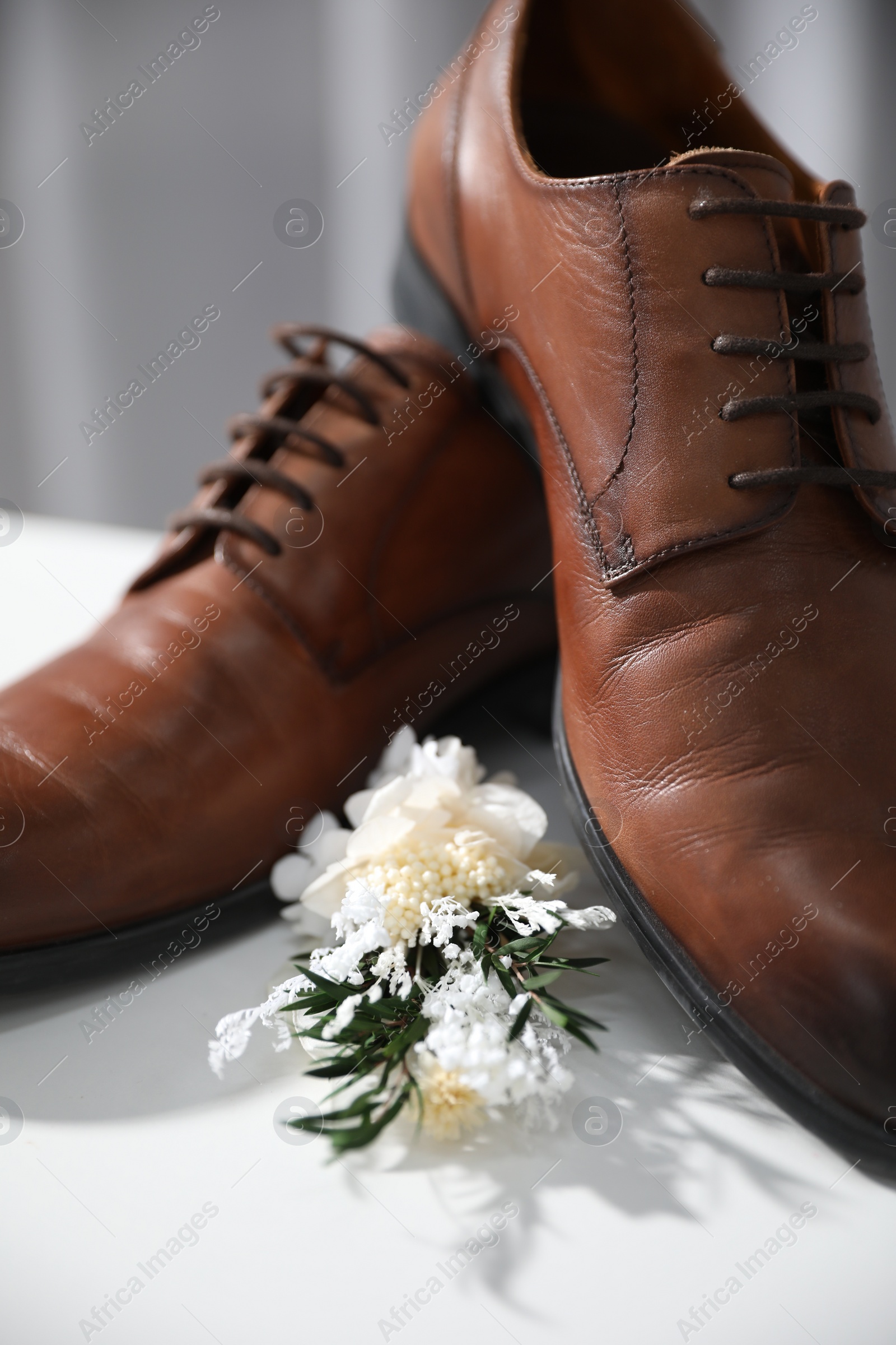 Photo of Wedding stuff. Stylish boutonniere and brown shoes on white surface, closeup