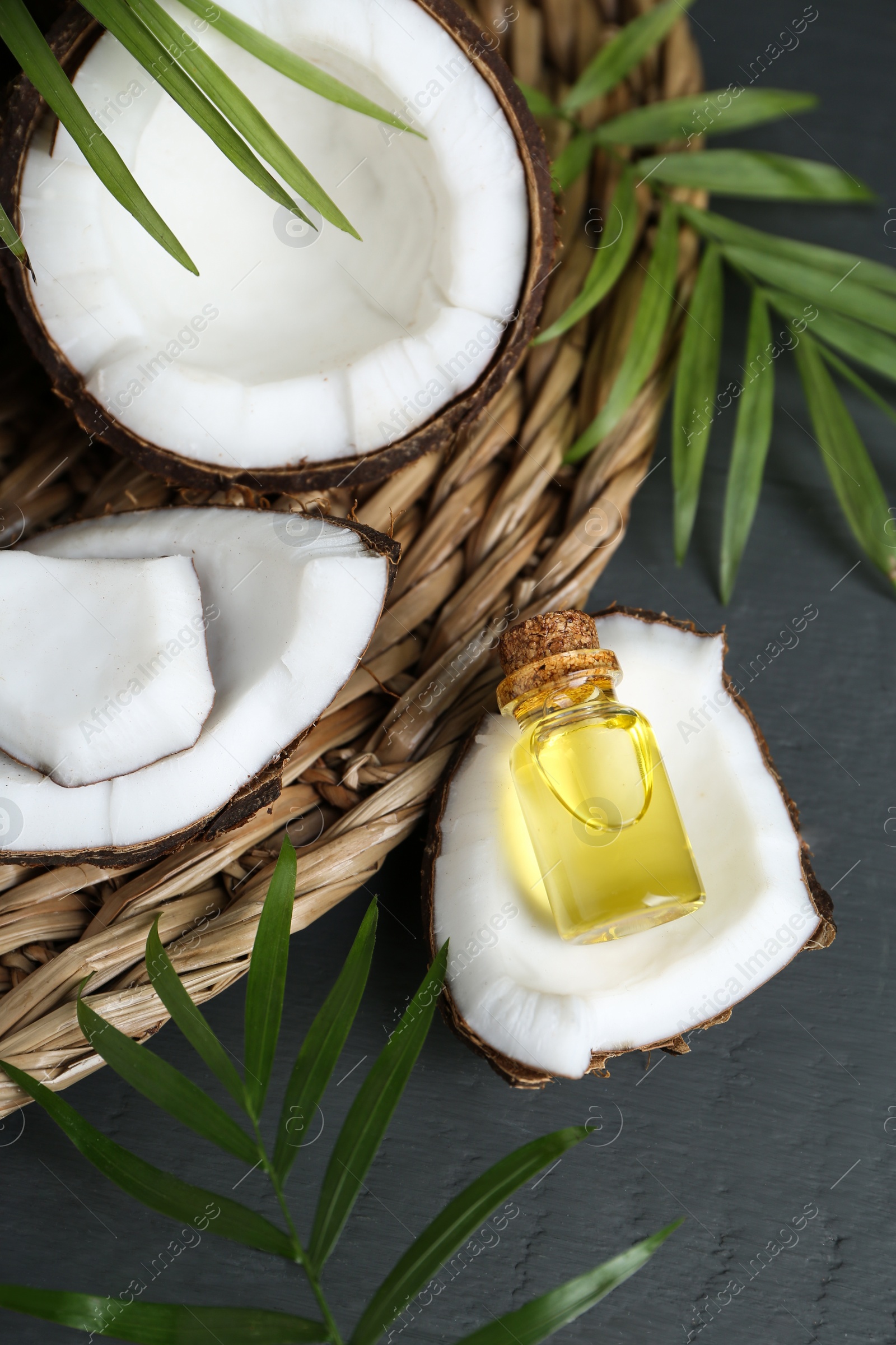 Photo of Bottle of organic coconut cooking oil, leaves and fresh fruits on grey wooden table, above view