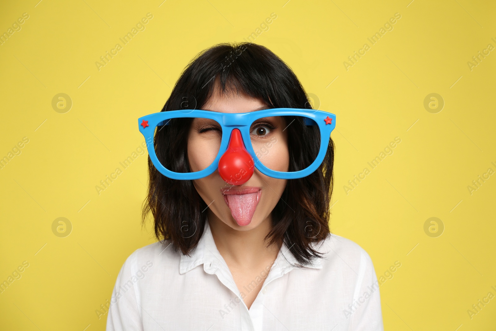 Photo of Joyful woman with funny glasses on yellow background. April fool's day