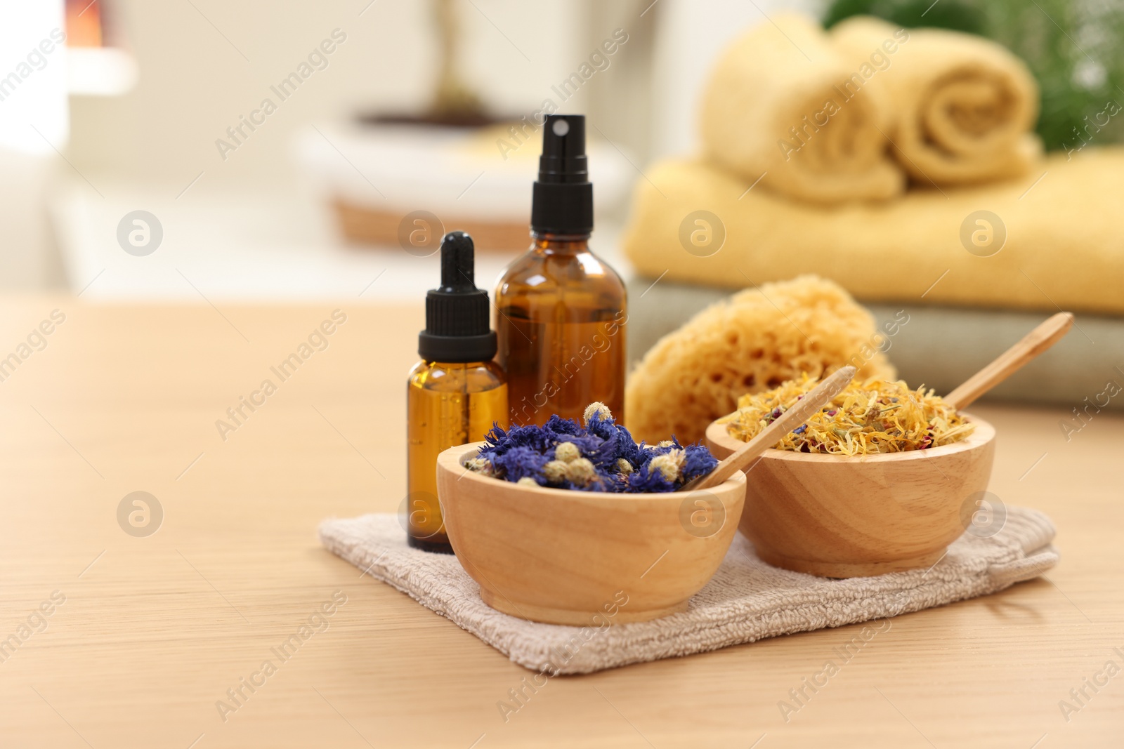 Photo of Bottles of essential oils, bowls with dry flowers and natural sponge on light wooden table, space for text. Spa therapy