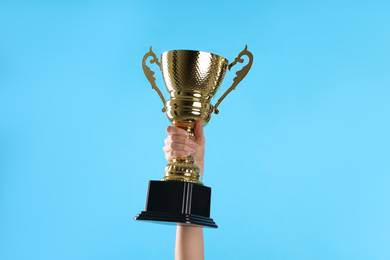 Photo of Woman holding gold trophy cup on light blue background, closeup