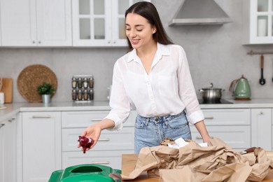 Photo of Garbage sorting. Smiling woman throwing onion peel into trash bin in kitchen