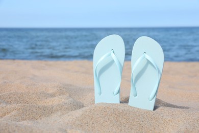 Stylish light blue flip flops on beach sand, space for text