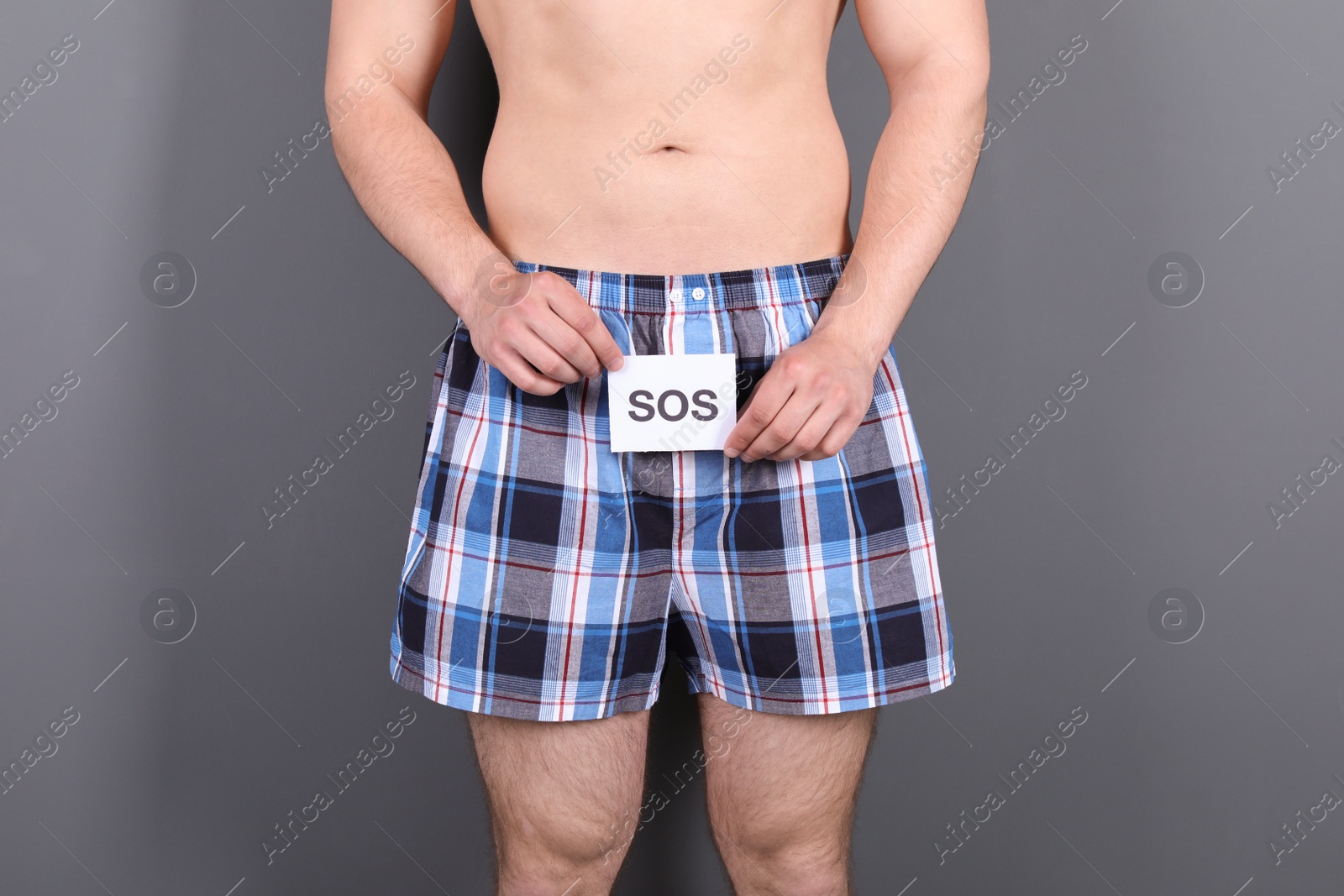 Photo of Young man with urological problems holding SOS sign on grey background