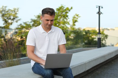 Photo of Handsome man using laptop on stone bench outdoors. Space for text