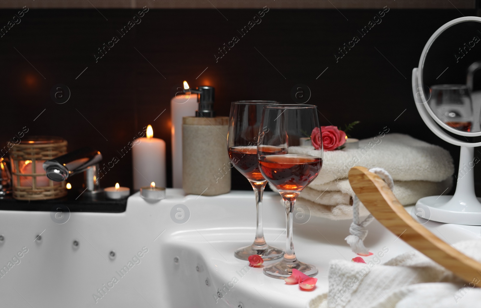 Photo of Bathtub with glasses of wine and candles indoors. Romantic atmosphere