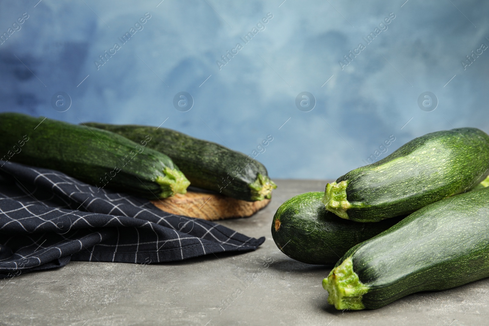 Photo of Fresh ripe green zucchinis on grey stone table against blue background, space for text