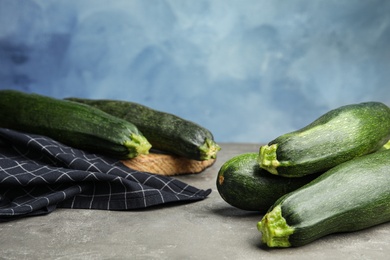 Photo of Fresh ripe green zucchinis on grey stone table against blue background, space for text