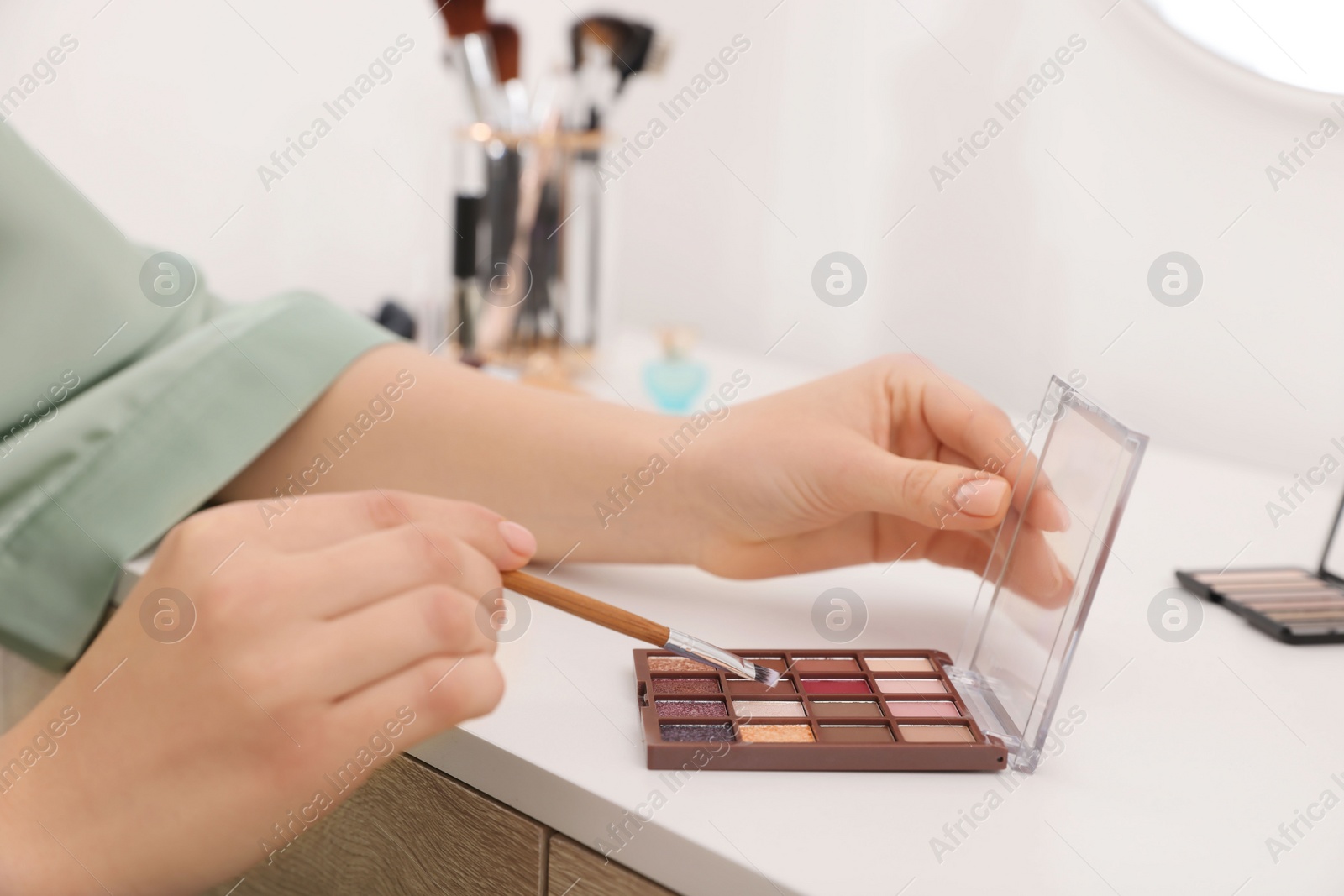 Photo of Woman with eyeshadow palette and brush at dressing table indoors, closeup